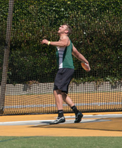 Athlete prepares for pole vault on a track with others watching.