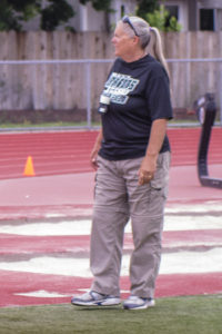 Athlete prepares for pole vault on a track with others watching.