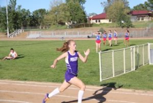 Athlete prepares for pole vault on a track with others watching.