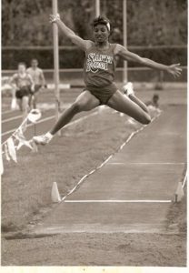 Athlete prepares for pole vault on a track with others watching.