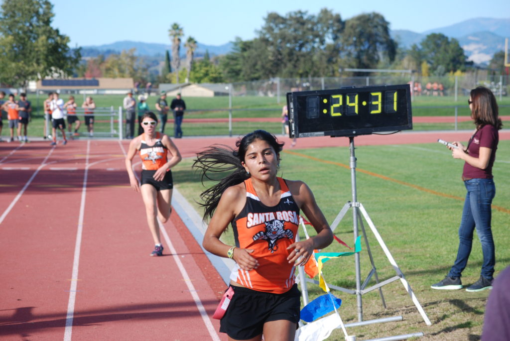 Athlete prepares for pole vault on a track with others watching.