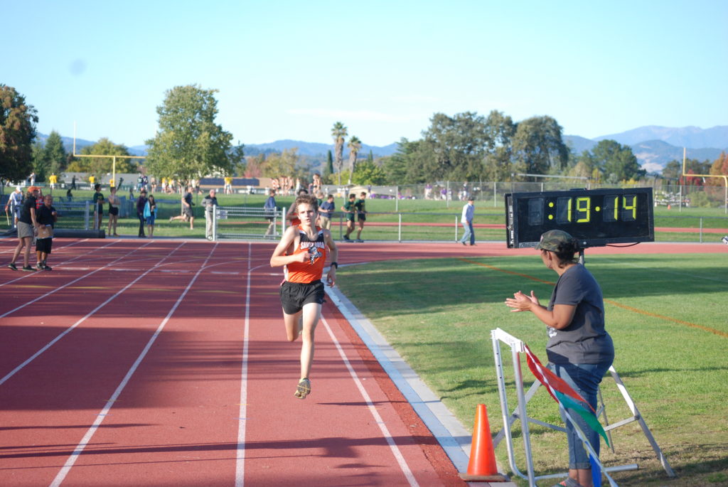 Athlete prepares for pole vault on a track with others watching.