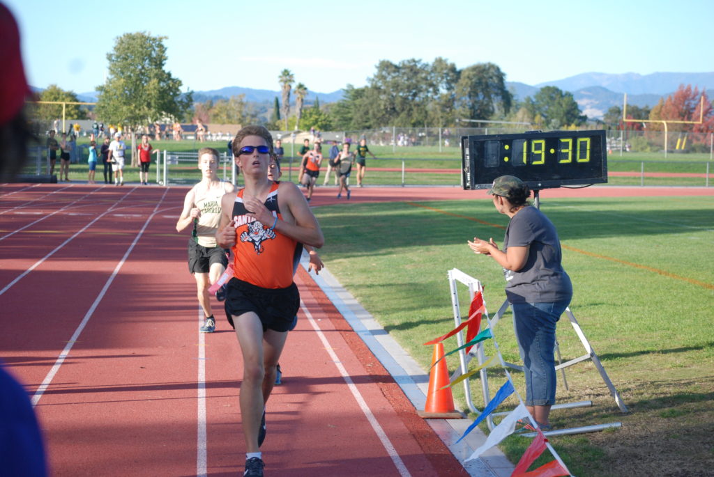Athlete prepares for pole vault on a track with others watching.