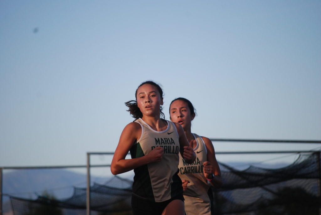 Athlete prepares for pole vault on a track with others watching.