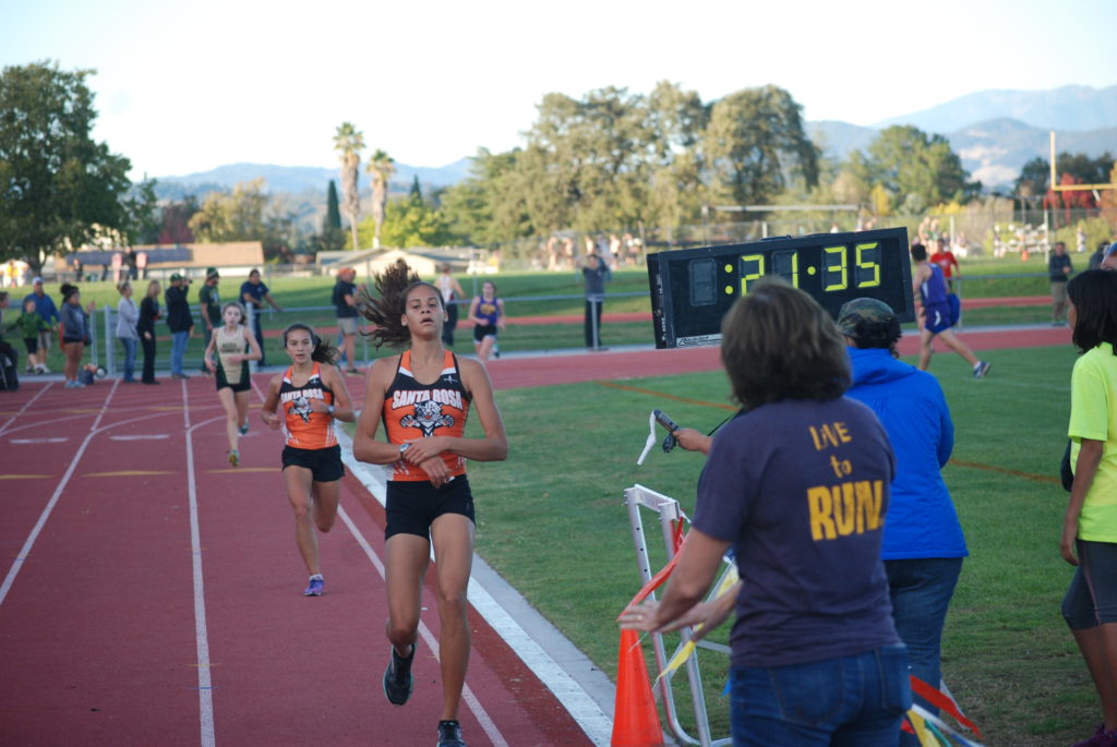 Athlete prepares for pole vault on a track with others watching.