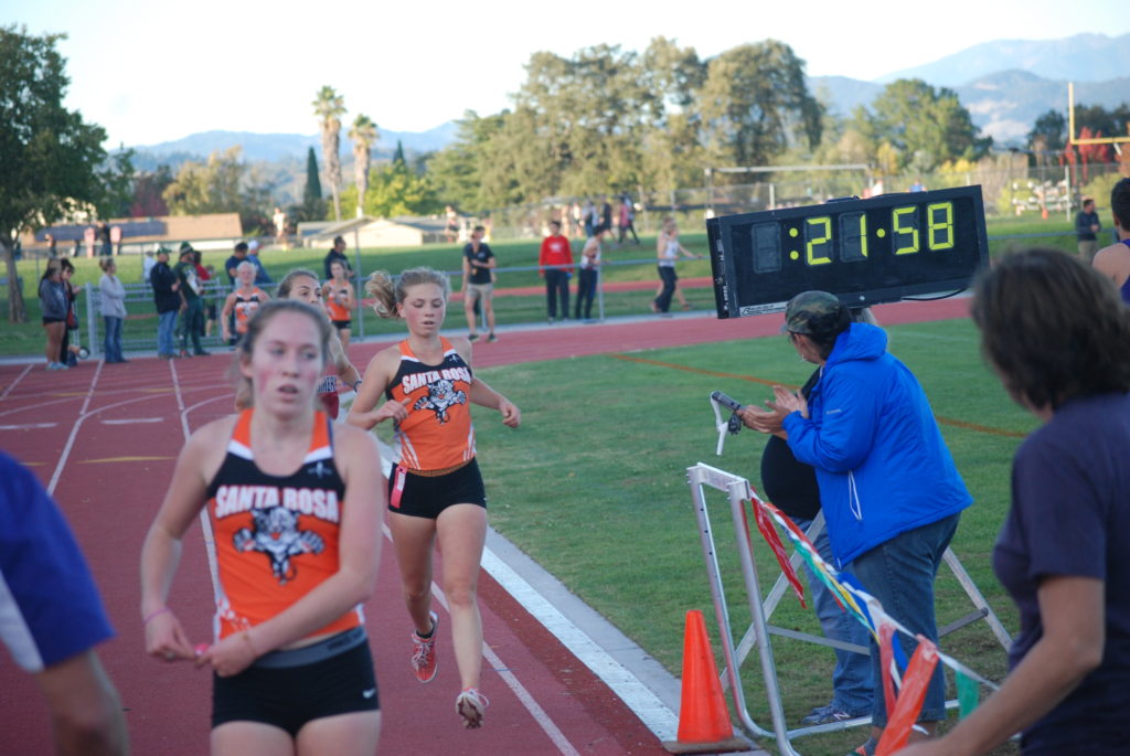Athlete prepares for pole vault on a track with others watching.