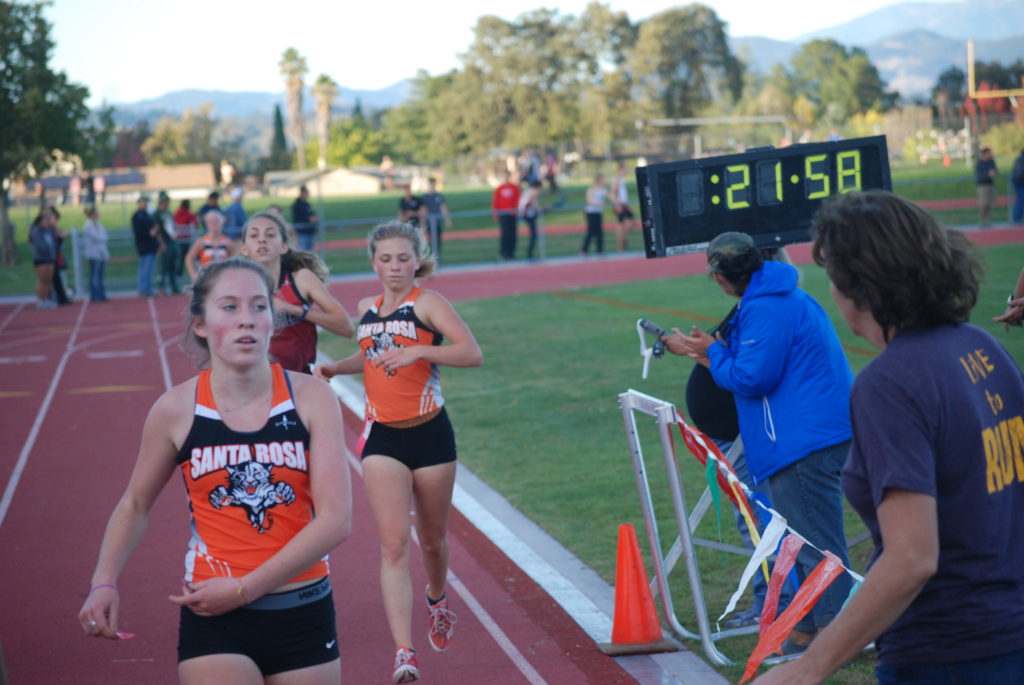 Athlete prepares for pole vault on a track with others watching.