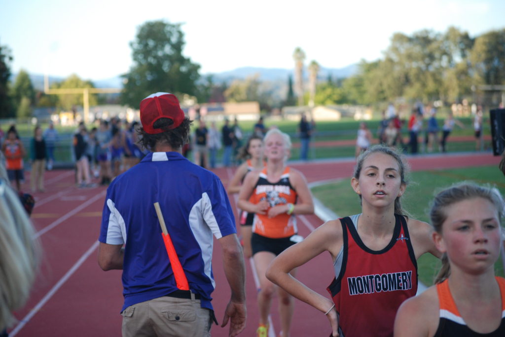 Athlete prepares for pole vault on a track with others watching.