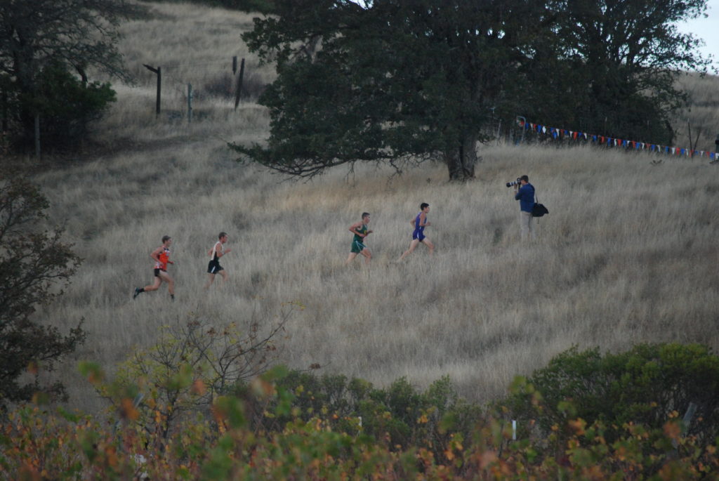 Athlete prepares for pole vault on a track with others watching.