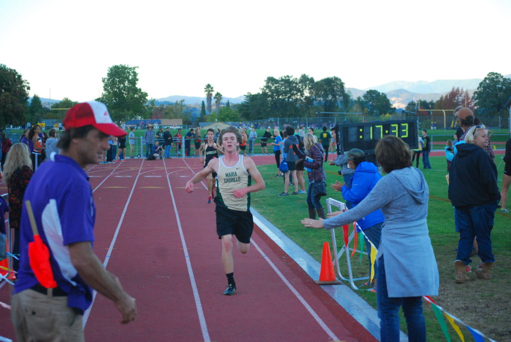 Athlete prepares for pole vault on a track with others watching.