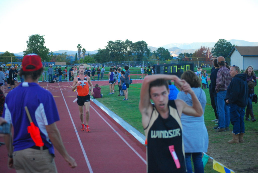 Athlete prepares for pole vault on a track with others watching.