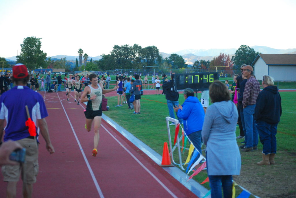 Athlete prepares for pole vault on a track with others watching.