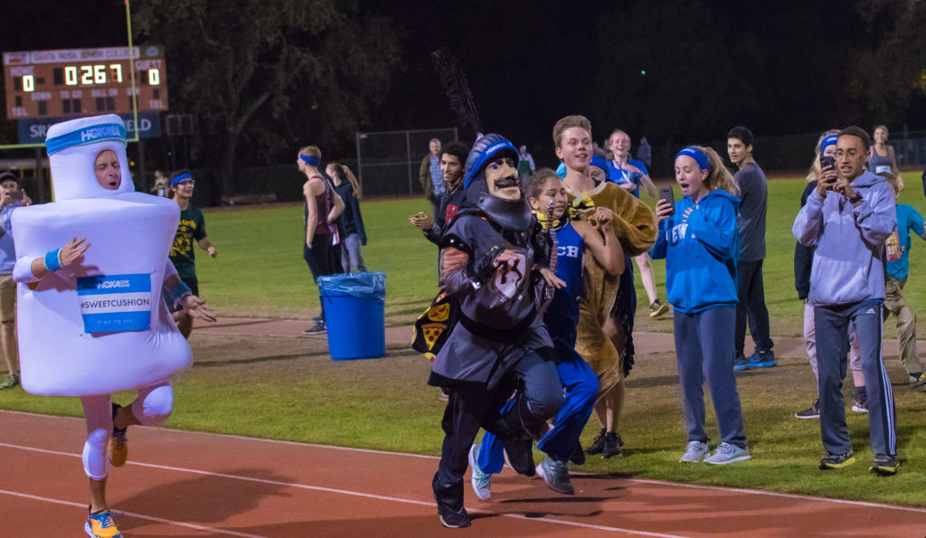 Athlete prepares for pole vault on a track with others watching.