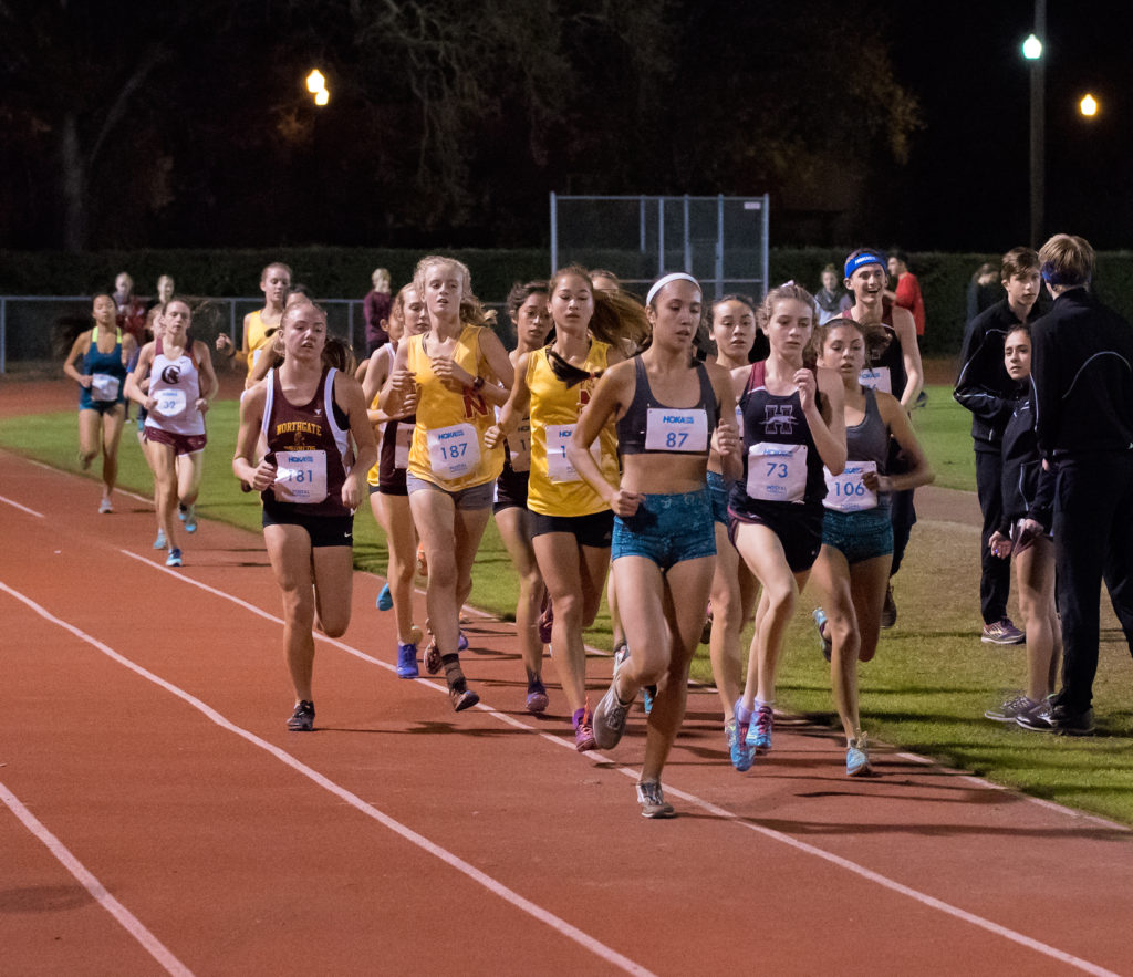 Athlete prepares for pole vault on a track with others watching.