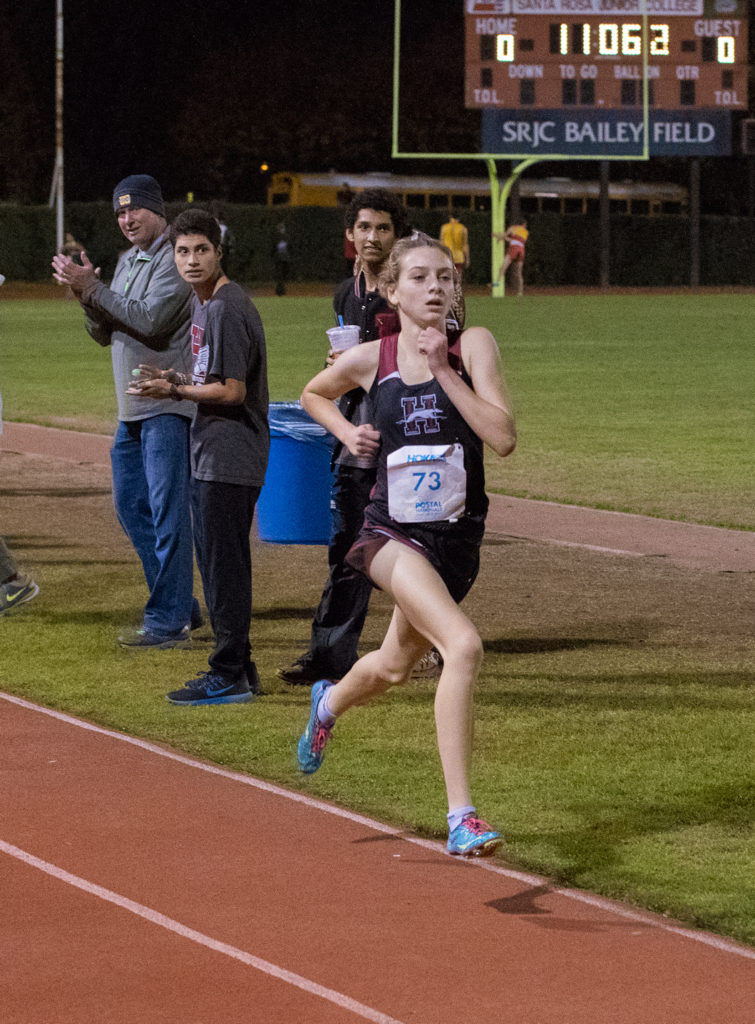 Athlete prepares for pole vault on a track with others watching.