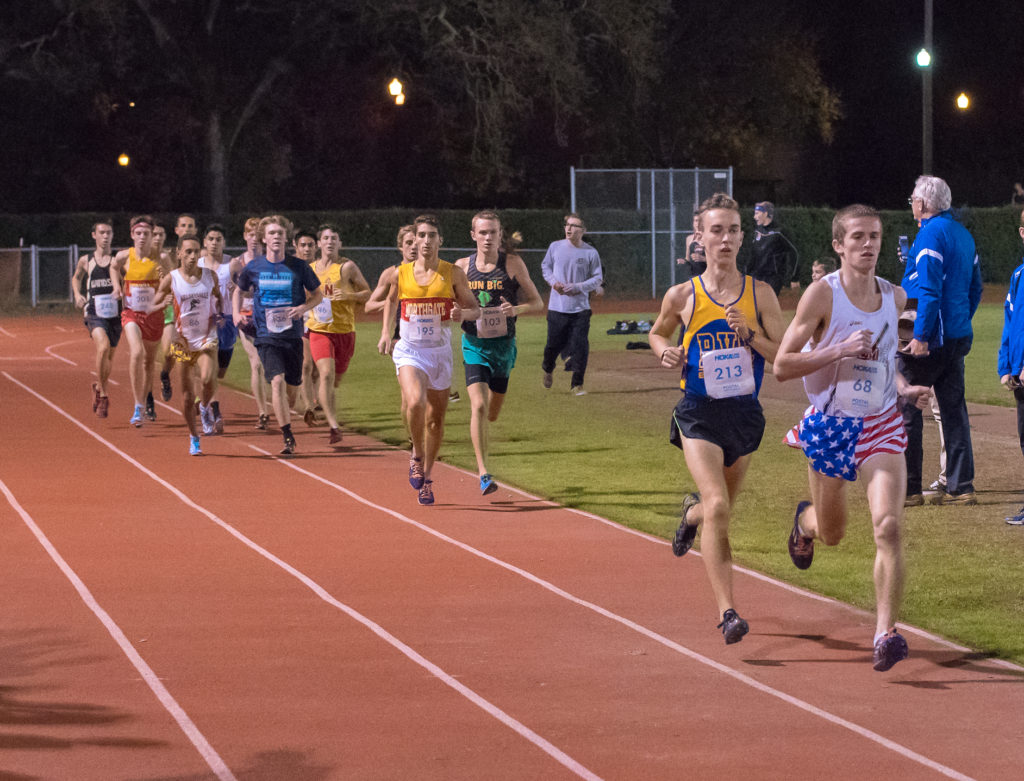Athlete prepares for pole vault on a track with others watching.
