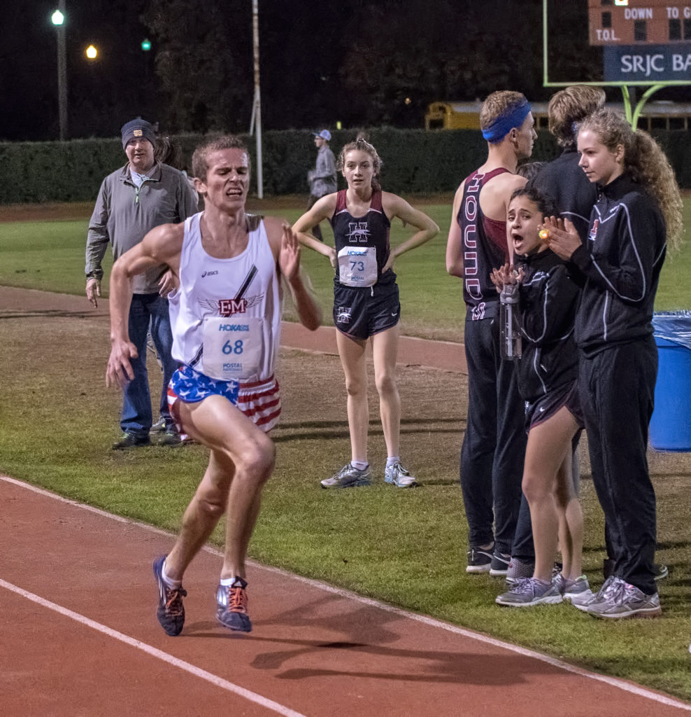 Athlete prepares for pole vault on a track with others watching.