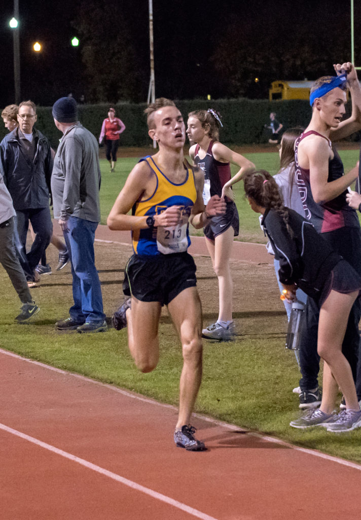Athlete prepares for pole vault on a track with others watching.