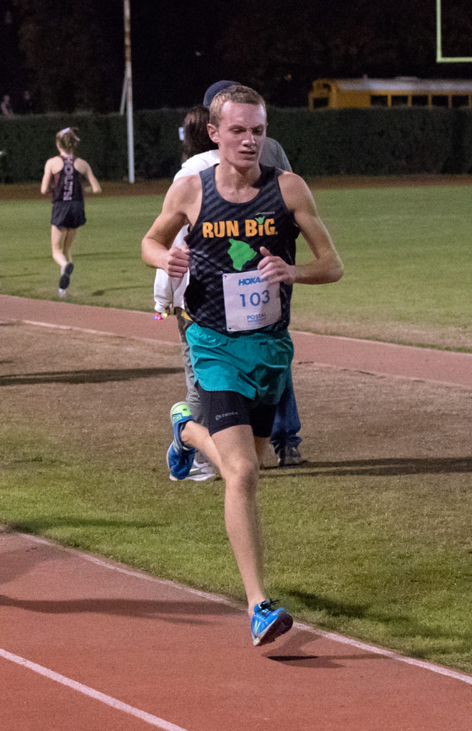 Athlete prepares for pole vault on a track with others watching.