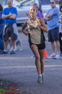 Athlete prepares for pole vault on a track with others watching.