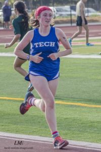 Athlete prepares for pole vault on a track with others watching.