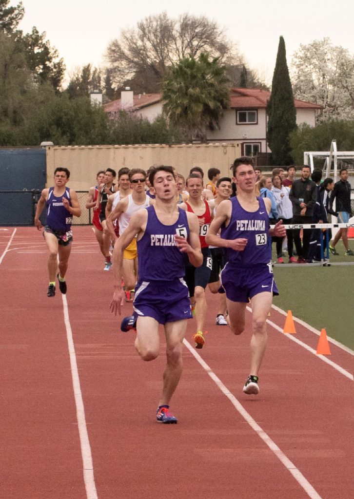 Athlete prepares for pole vault on a track with others watching.