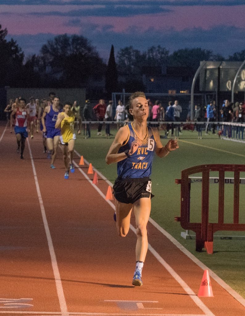 Athlete prepares for pole vault on a track with others watching.