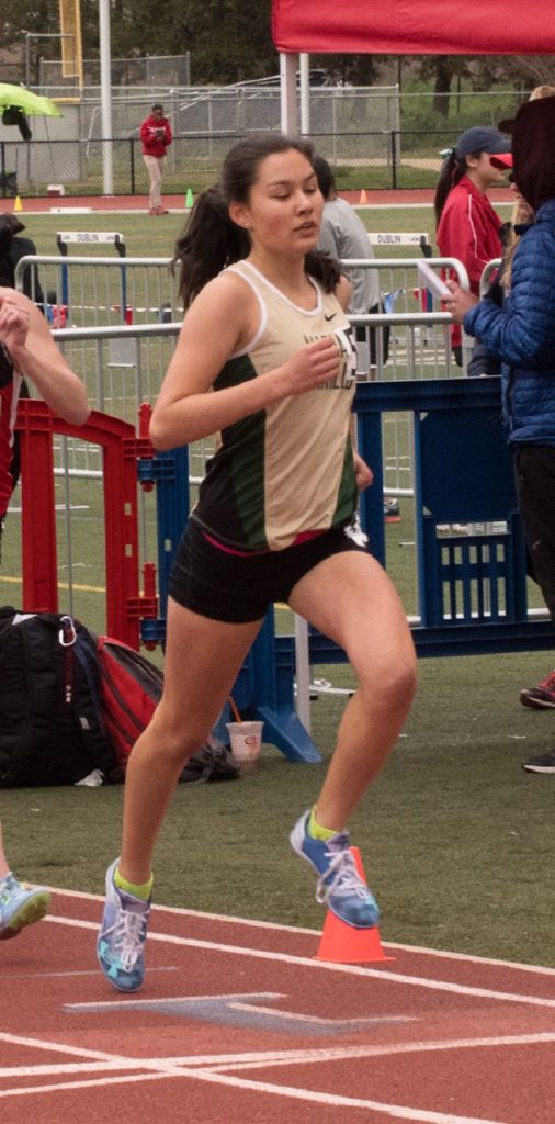 Athlete prepares for pole vault on a track with others watching.