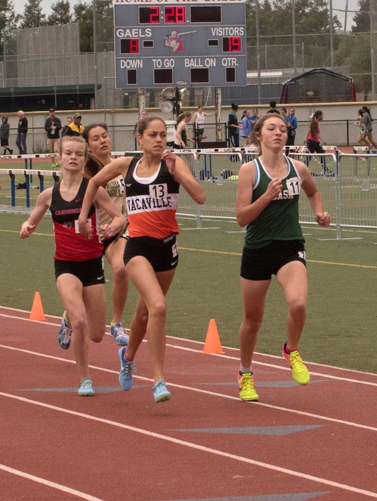 Athlete prepares for pole vault on a track with others watching.