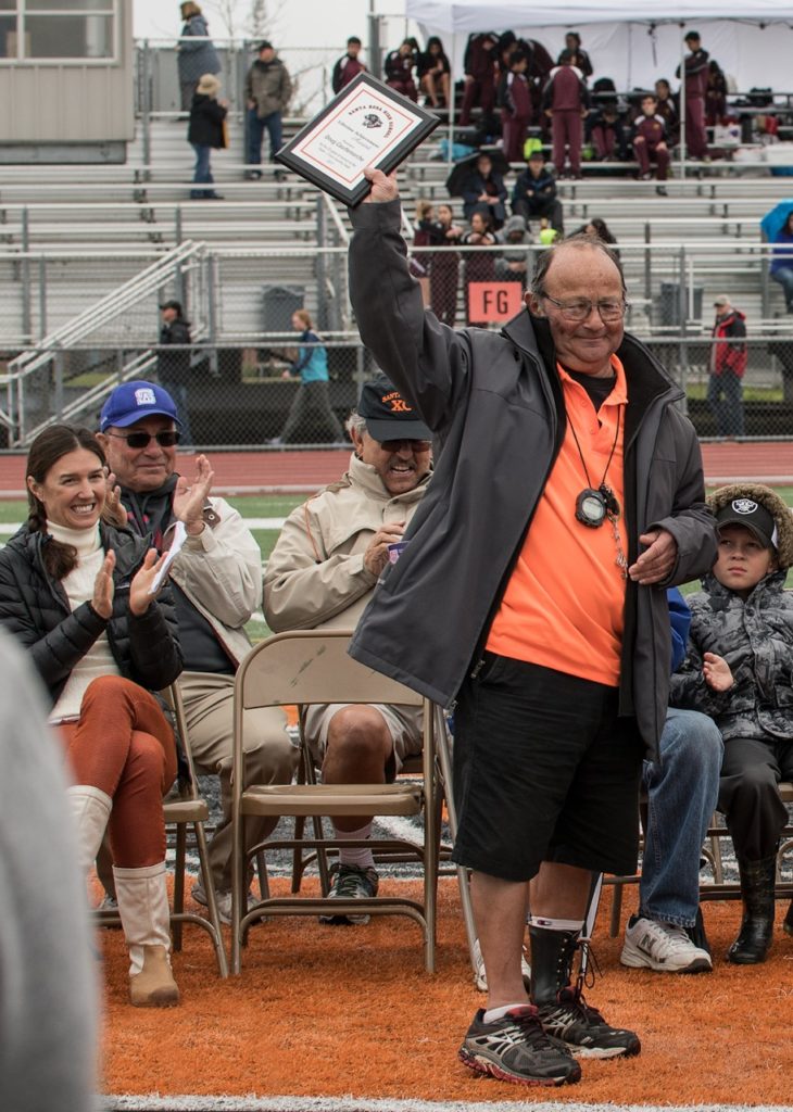 Athlete prepares for pole vault on a track with others watching.