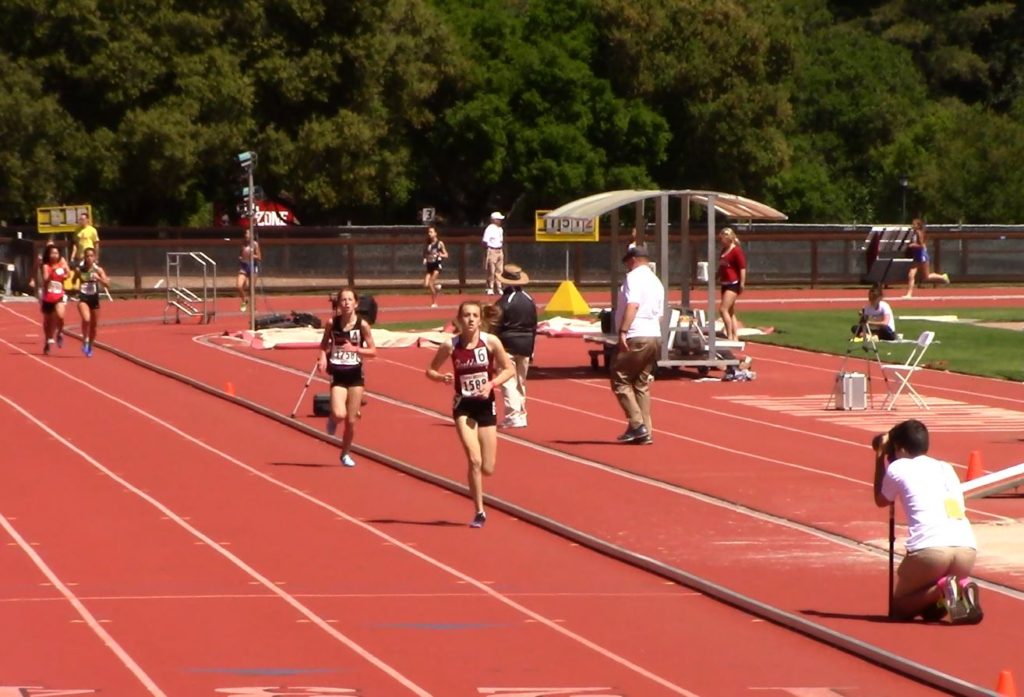 Athlete prepares for pole vault on a track with others watching.