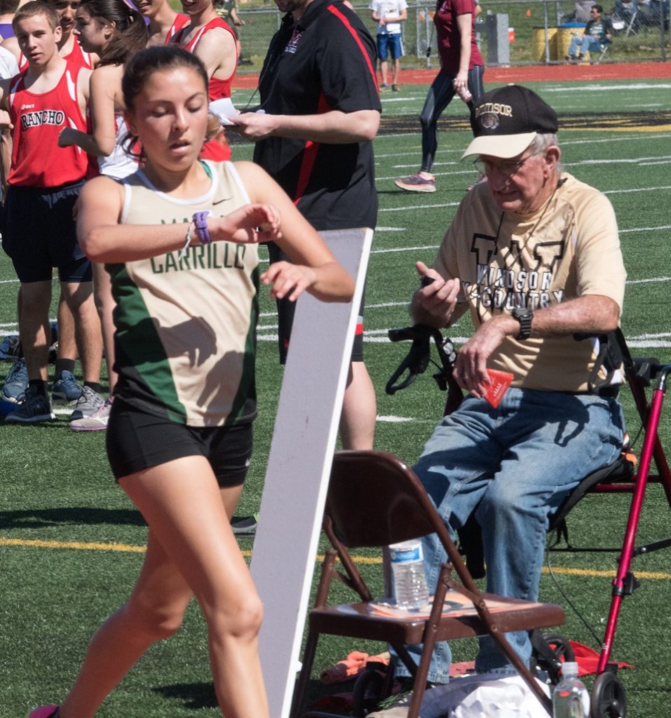 Athlete prepares for pole vault on a track with others watching.