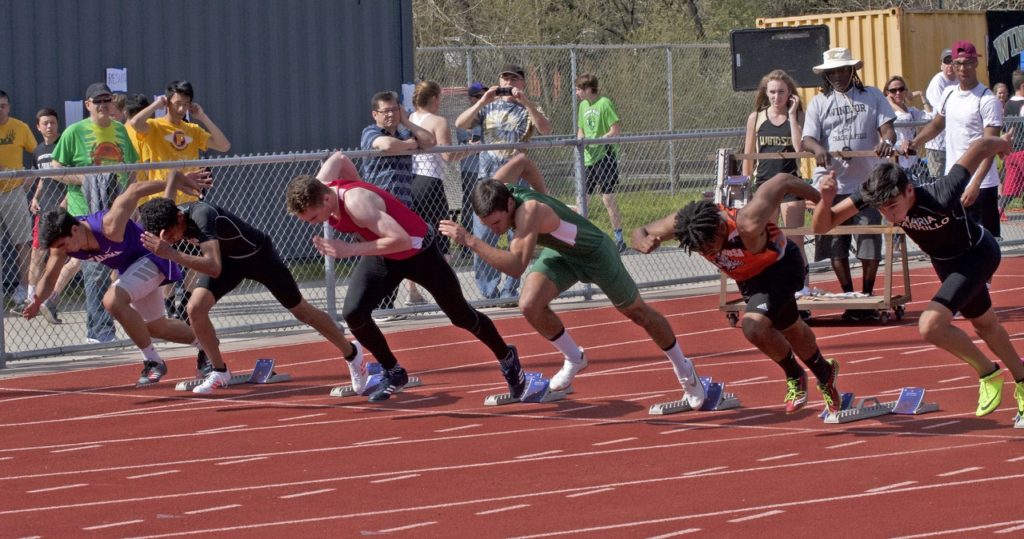 Athlete prepares for pole vault on a track with others watching.