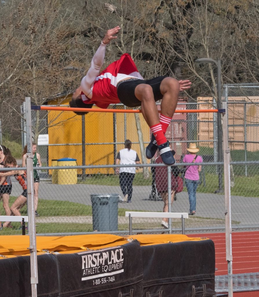 Athlete prepares for pole vault on a track with others watching.