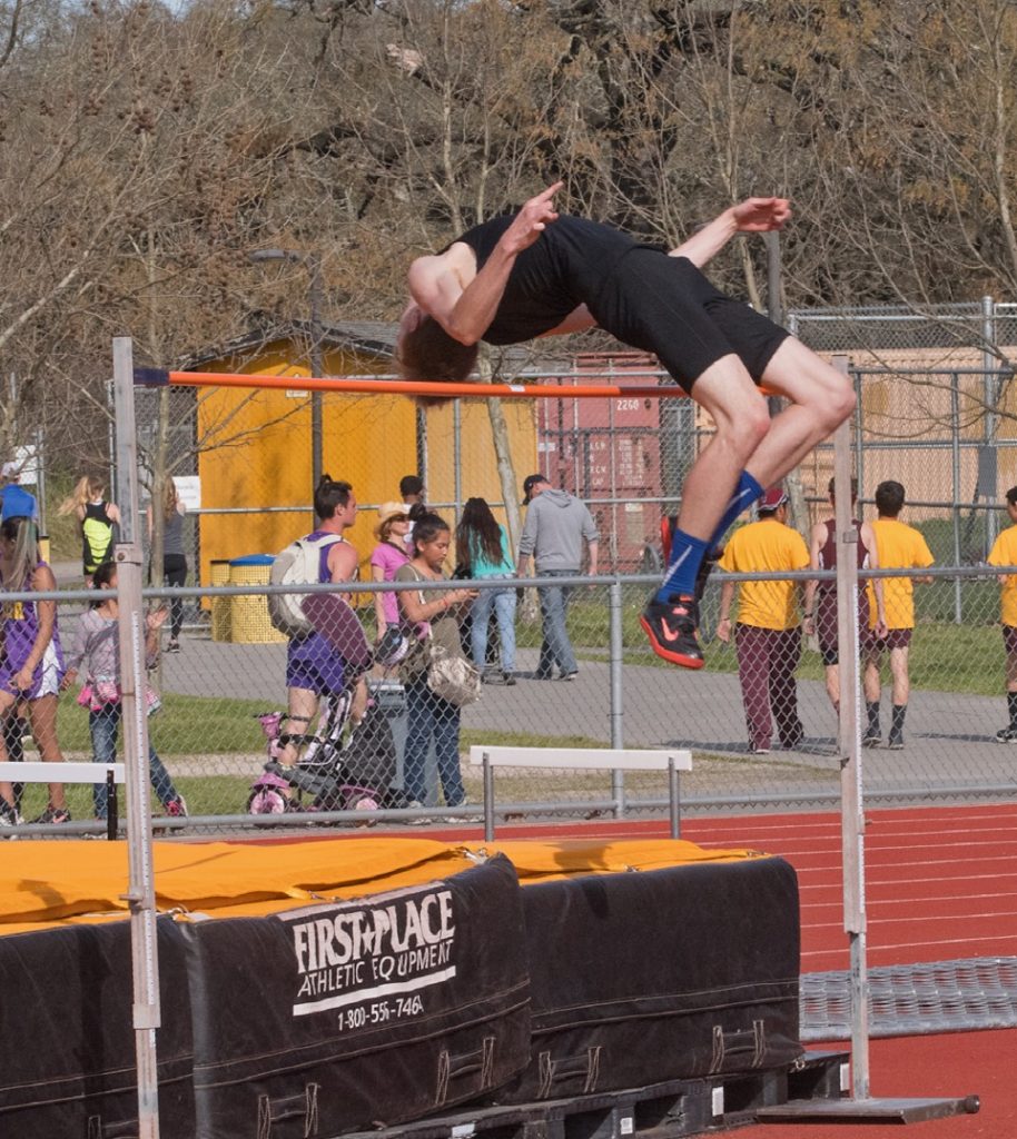 Athlete prepares for pole vault on a track with others watching.