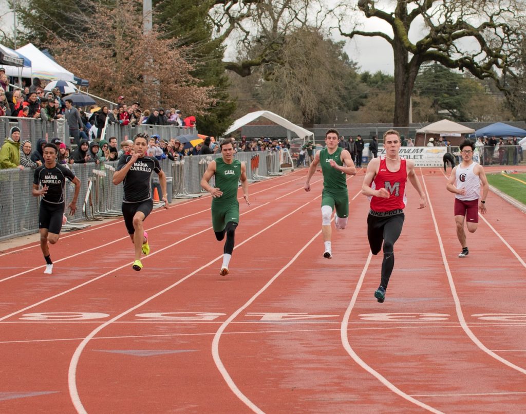 Athlete prepares for pole vault on a track with others watching.
