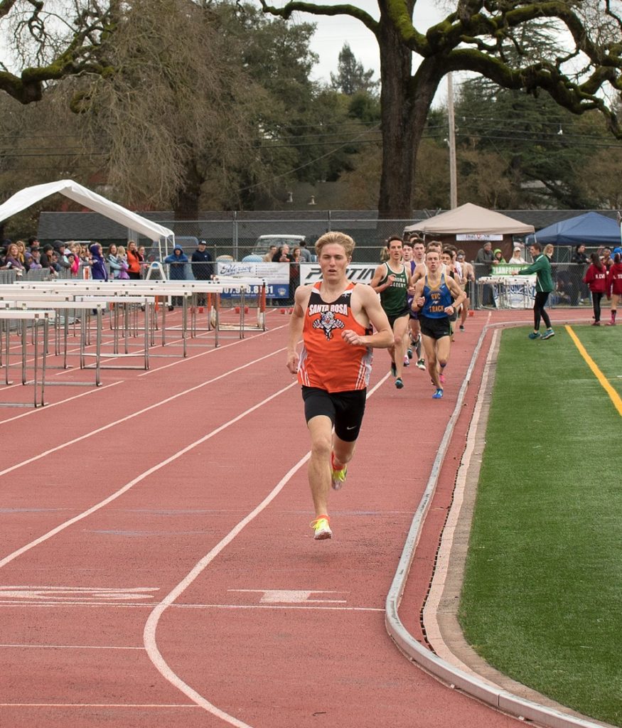 Athlete prepares for pole vault on a track with others watching.
