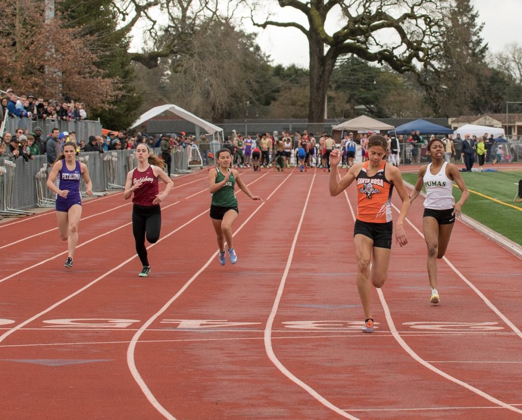 Athlete prepares for pole vault on a track with others watching.