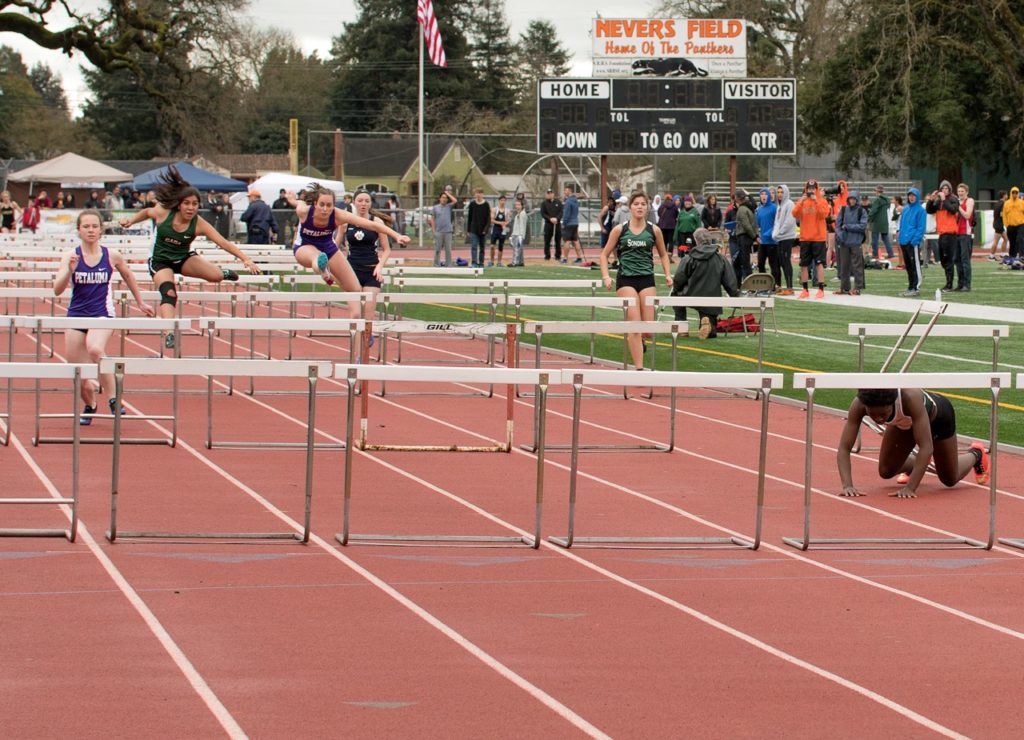 Athlete prepares for pole vault on a track with others watching.