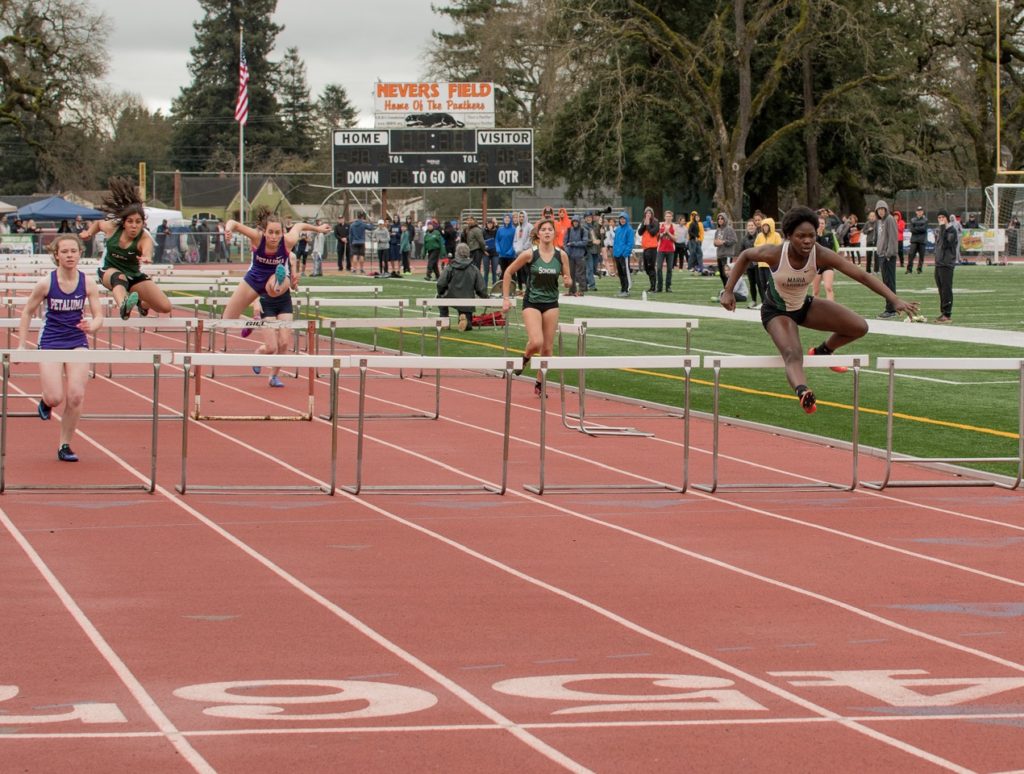 Athlete prepares for pole vault on a track with others watching.