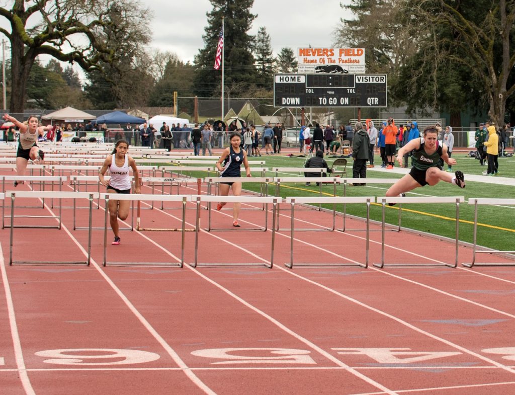 Athlete prepares for pole vault on a track with others watching.