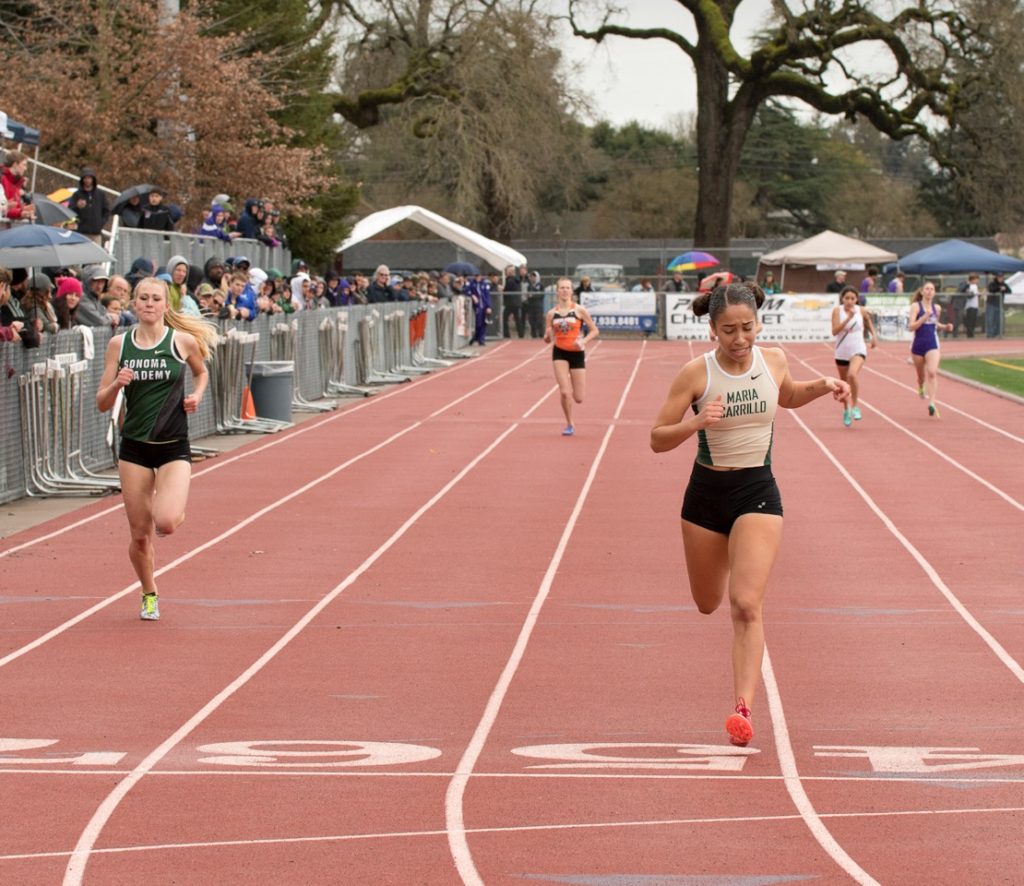 Athlete prepares for pole vault on a track with others watching.