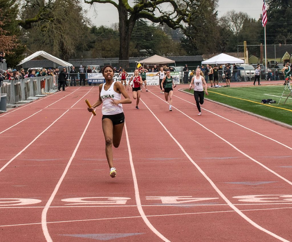 Athlete prepares for pole vault on a track with others watching.