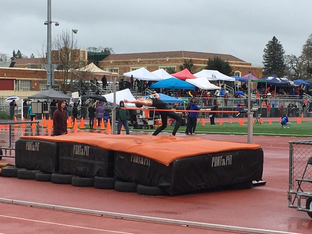Athlete prepares for pole vault on a track with others watching.