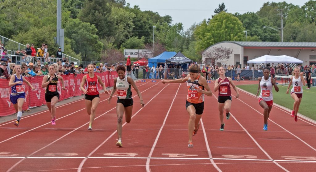 Athlete prepares for pole vault on a track with others watching.