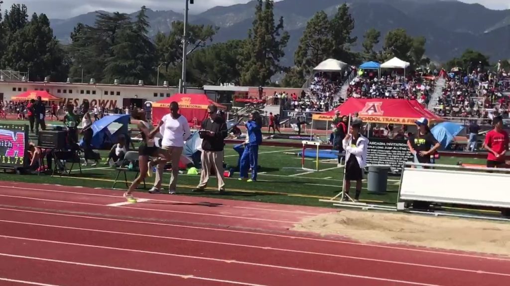 Athlete prepares for pole vault on a track with others watching.