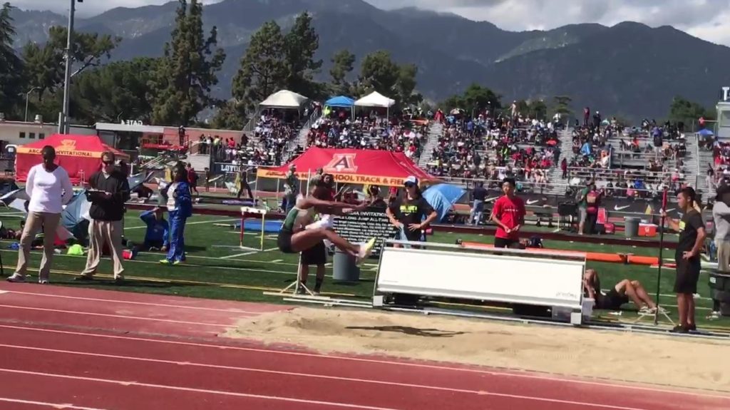 Athlete prepares for pole vault on a track with others watching.