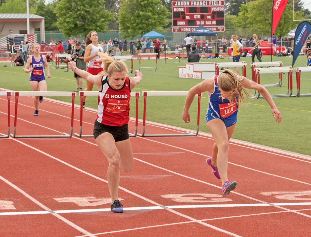 Athlete prepares for pole vault on a track with others watching.