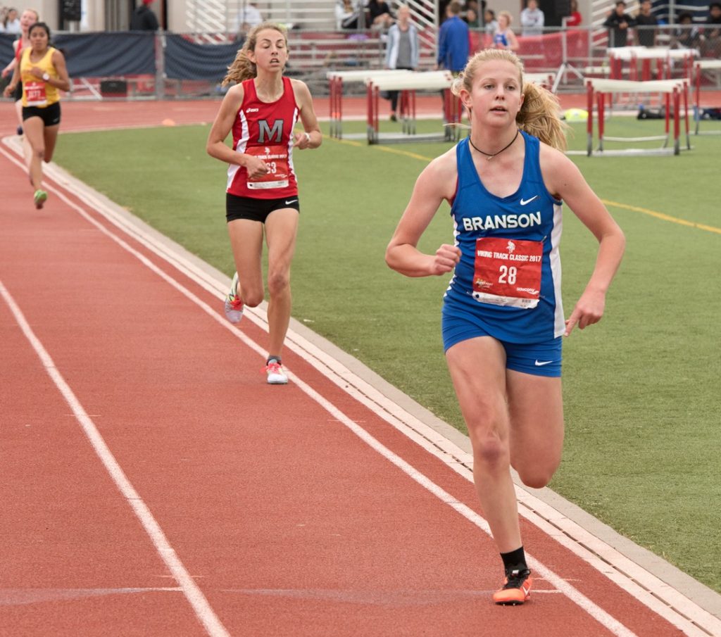 Athlete prepares for pole vault on a track with others watching.