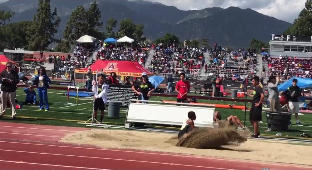Athlete prepares for pole vault on a track with others watching.